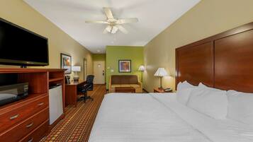 A hotel room with a large bed, a desk with a computer, a television, and a ceiling fan.