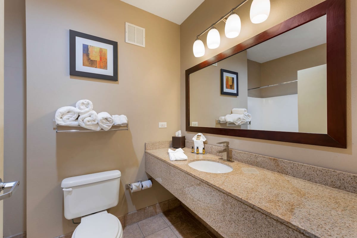 A bathroom with a toilet, sink, towel rack, and a large mirror with lights.