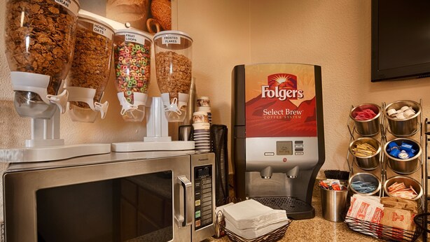 A coffee station with a Folgers Select Brew coffee system, various coffee pods, and a cereal dispenser with options like honey oats and fruit loops. - Super 8 by Wyndham McGehee (McGehee)