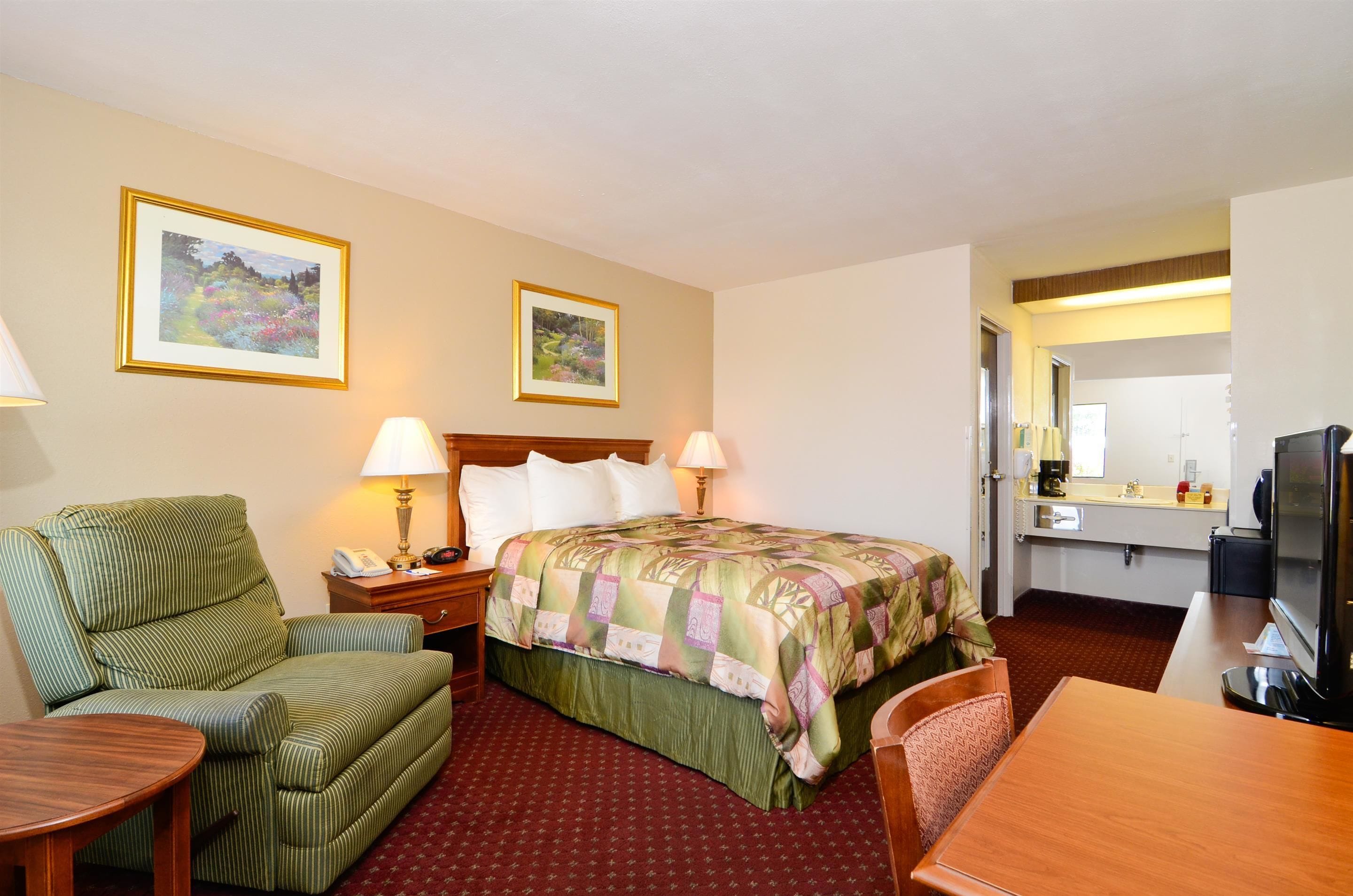 Una habitación de hotel con una cama, un sofá, un escritorio y una mesa de comedor. Hay dos lámparas en las mesitas de noche, un teléfono y un televisor sobre el escritorio.