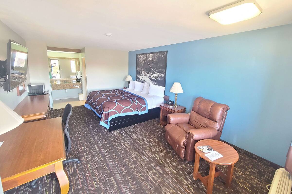A hotel room with a bed, a desk, a chair, and a small table.