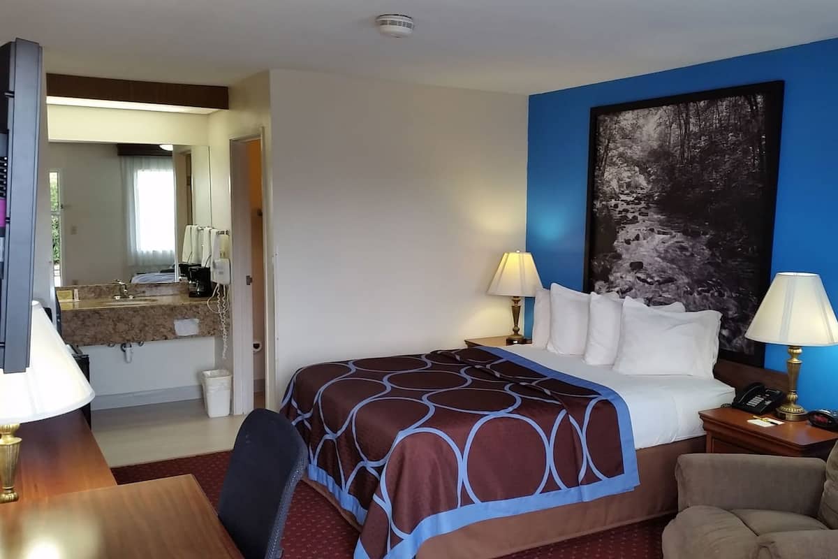 A hotel room with a bed, two bedside lamps, a desk with a telephone, a chair, and a large painting on the wall.