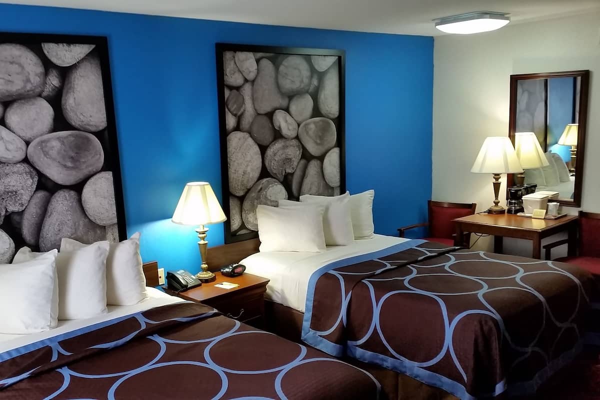 A hotel room with two beds, a nightstand with a lamp, a coffee maker, and a mirror.