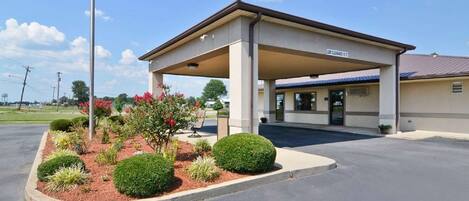A gas station with a covered canopy, a landscaped garden with various plants and flowers, and a clear sky.