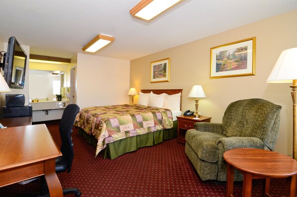 Habitación de hotel con cama, escritorio, silla, lámpara y dos cuadros en la pared.