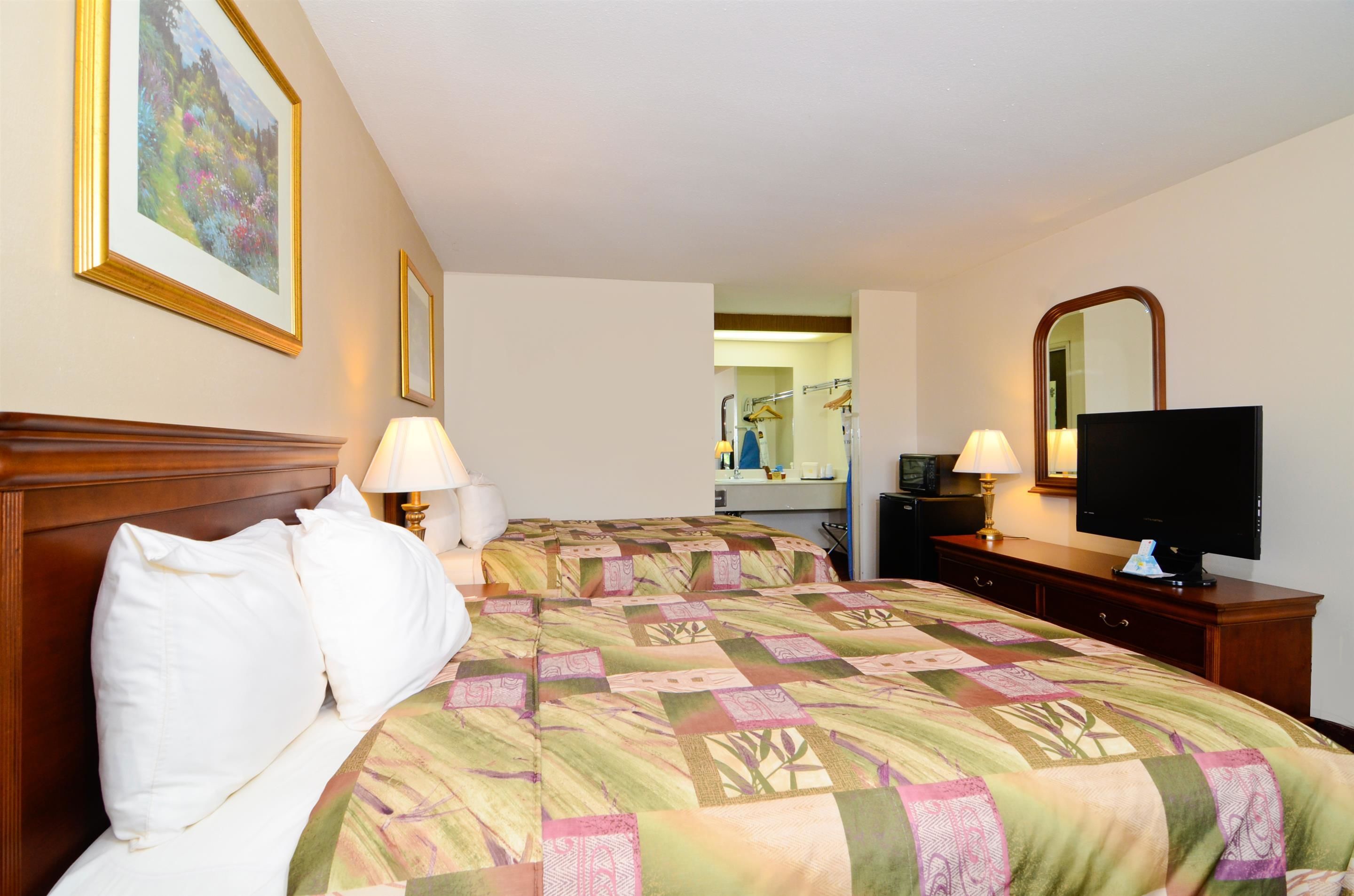 A hotel room with a large bed, two bedside lamps, a television, and a mirror.