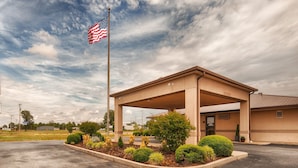 A motel with a covered parking area, a flagpole with an American flag, and a well-maintained garden. - Super 8 by Wyndham McGehee (McGehee)