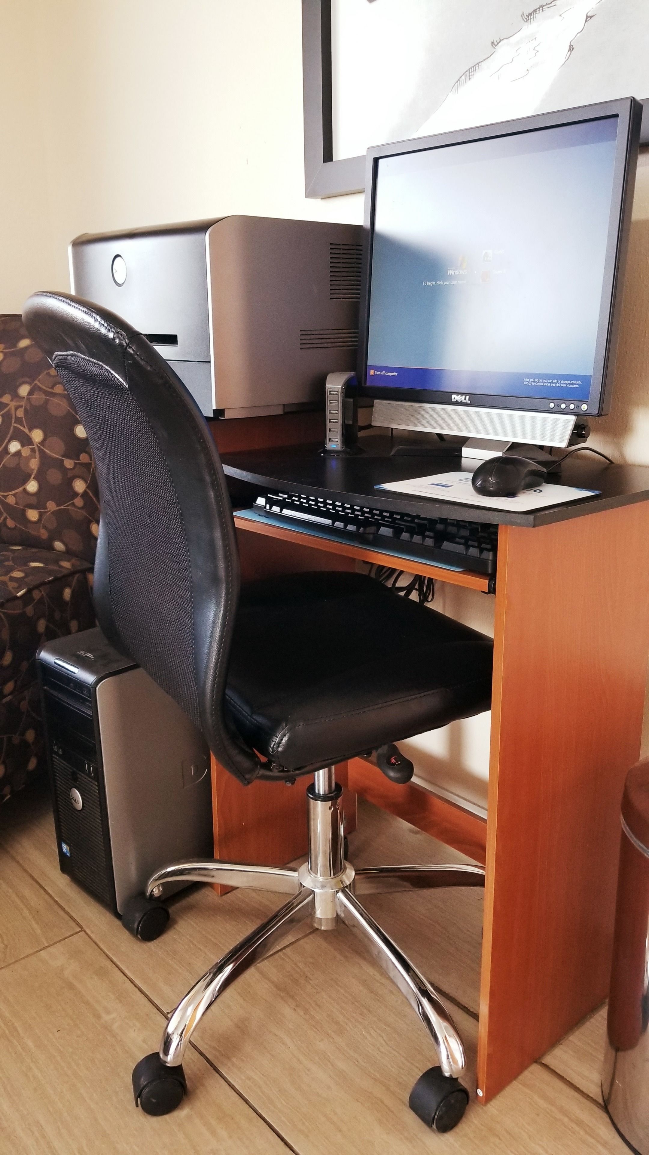 Un escritorio de madera con una computadora de escritorio Dell, una silla de oficina negra e impresora.