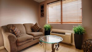 A living room with a brown sofa, two patterned cushions, a glass coffee table, and two potted plants. - Super 8 by Wyndham McGehee (McGehee)