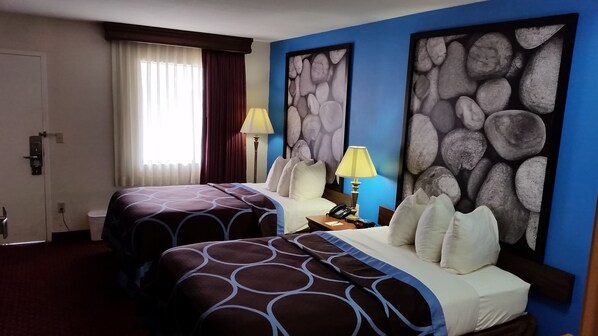 A hotel room with two beds, a nightstand, a lamp, and artwork on the walls. - Super 8 by Wyndham McGehee (McGehee)