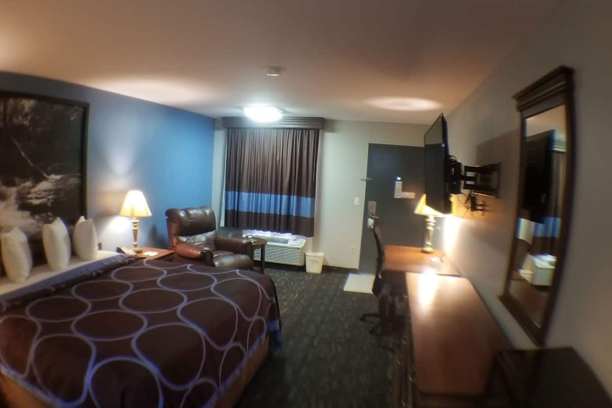 A hotel room with a bed, a desk, a chair, a lamp, a mirror, and a window with curtains.