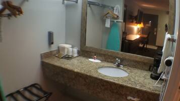 Un baño con encimera de granito, un lavabo, un espejo, toallero, un pequeño cubo de basura y una zona de ducha.