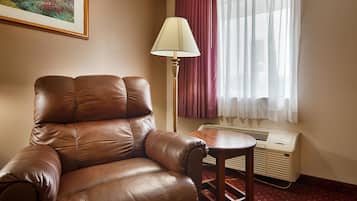 Una armchair de cuir marró amb una taula auxiliar de fusta, una làmpada de peu i una finestra amb cortines.