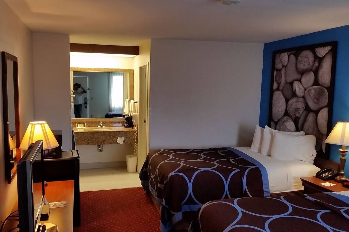 A hotel room with a bed, bedside table, lamp, and a bathroom visible through an open door.