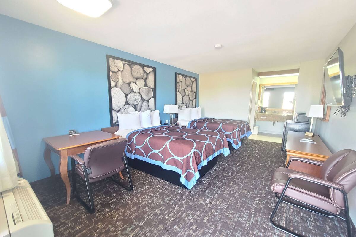 A hotel room with two beds, a desk, a chair, a lamp, and a large mirror.