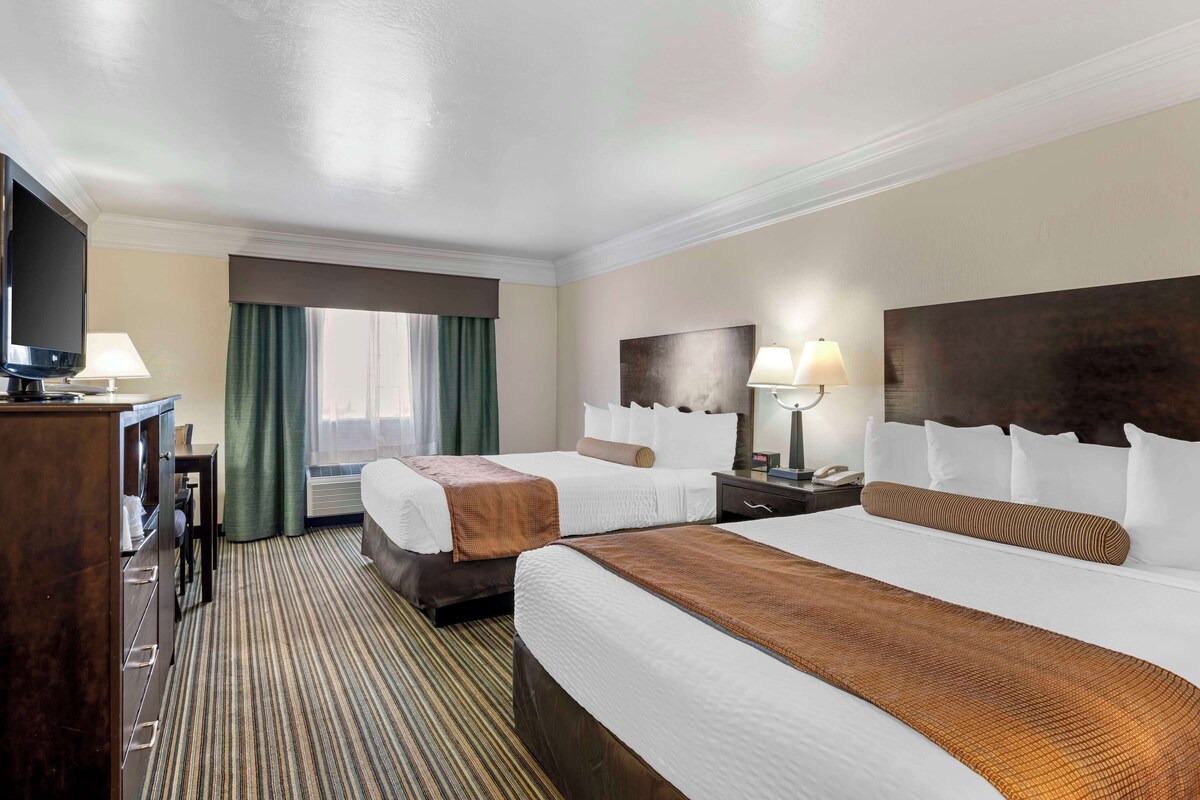 Une chambre d’hôtel avec deux lits, un bureau, une télévision et une fenêtre avec des rideaux.