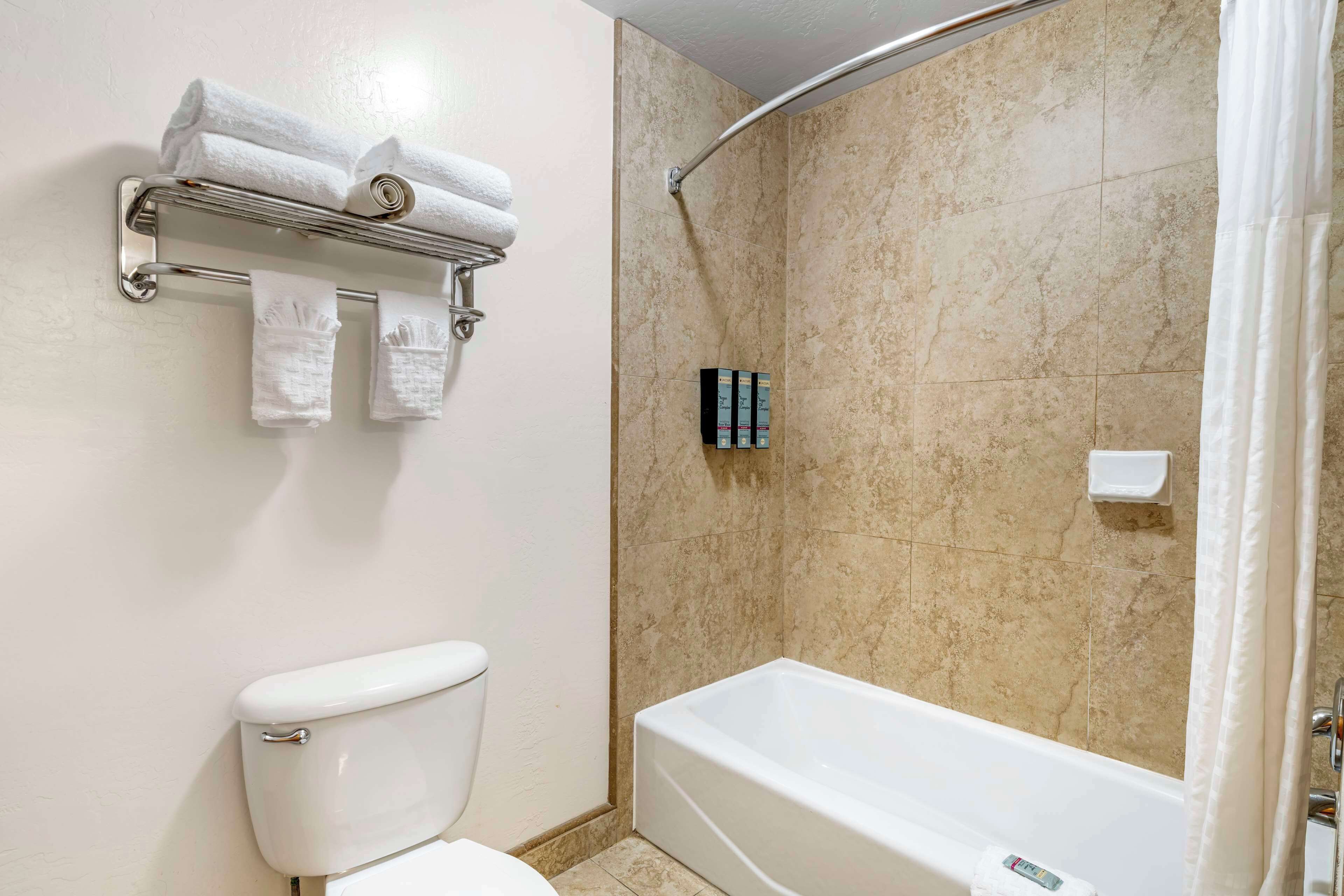 A bathroom with a toilet, a bathtub, a shower, and a towel rack with towels.