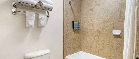 A bathroom with a toilet, a bathtub, a shower, and a towel rack with towels.