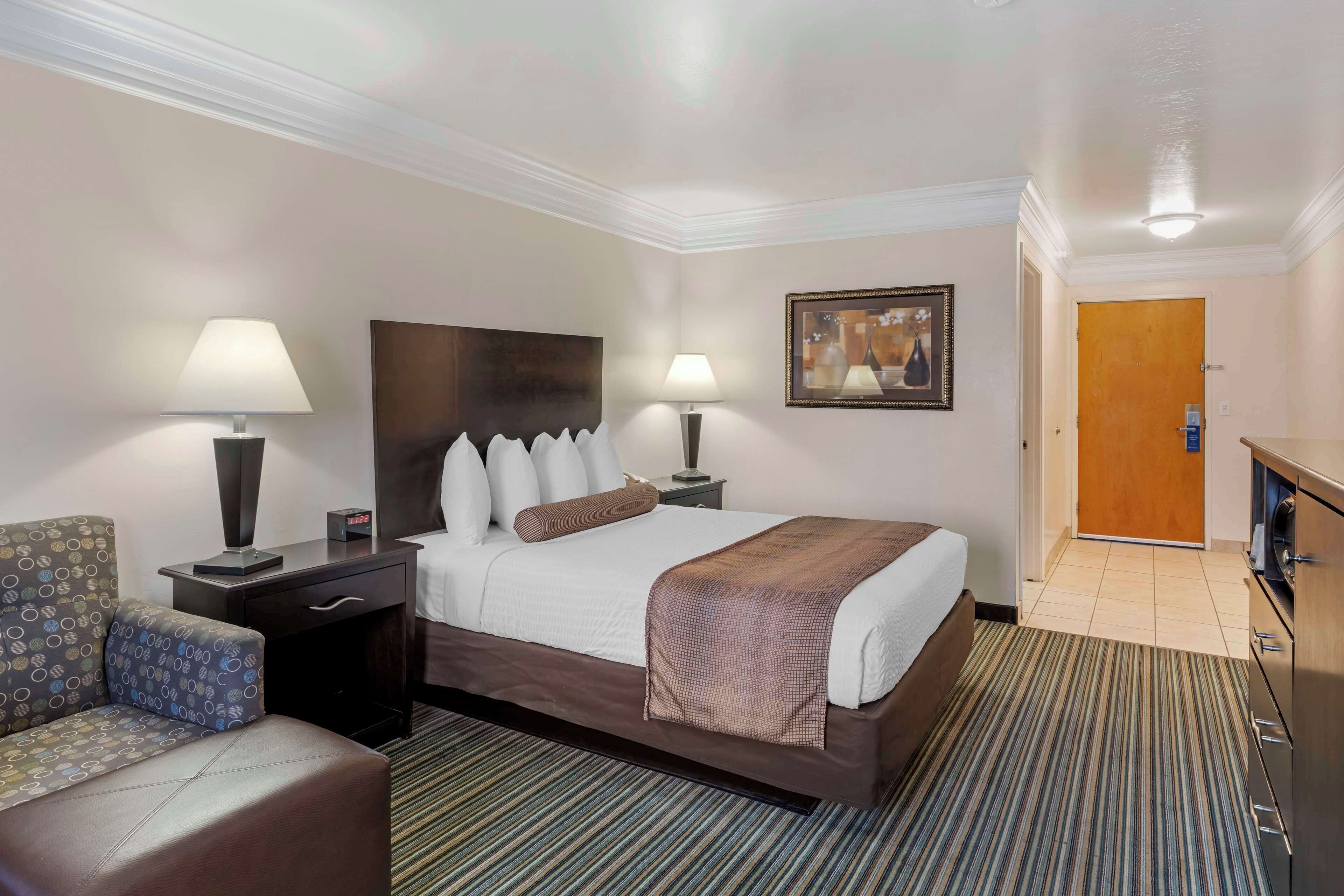 A hotel room with a large bed, two bedside tables with lamps, a chair, a desk, and a door leading to the bathroom.