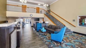 A spacious lobby with a reception desk, seating area, staircase, and a large clock.