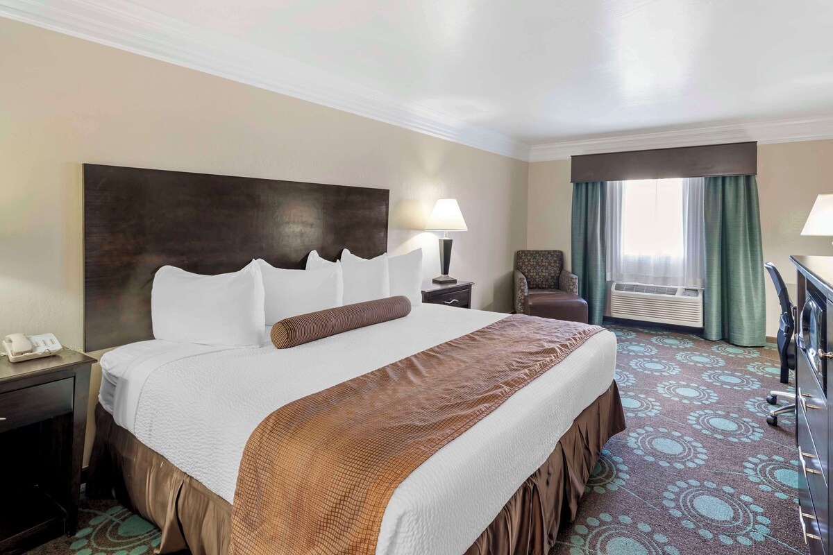 Une chambre d’hôtel avec un grand lit, un bureau, une chaise et une fenêtre avec des rideaux.
