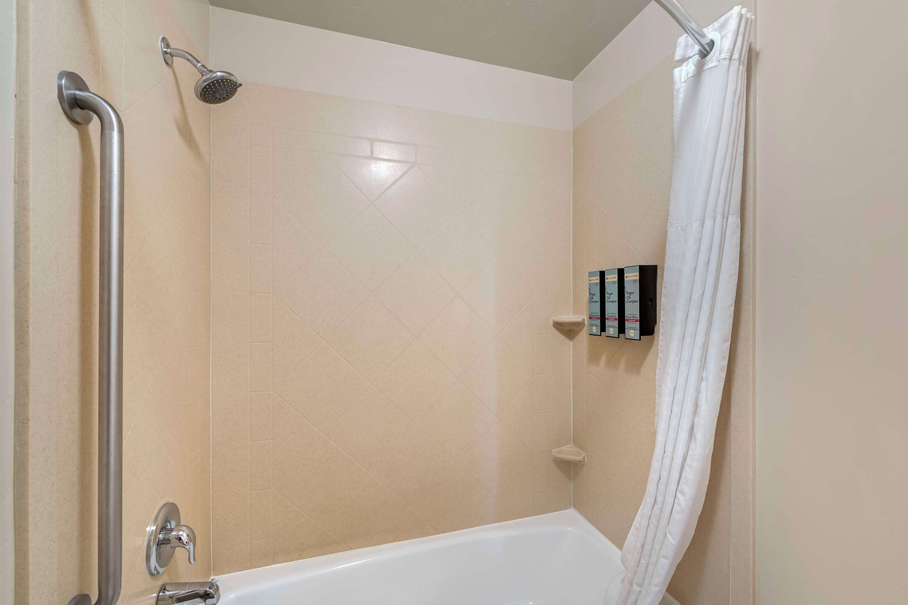 A bathroom with a shower, a grab bar, a white bathtub, and a white shower curtain.