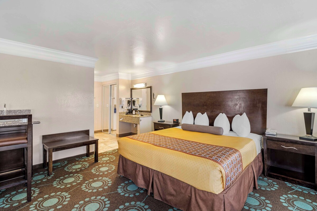 Une chambre d’hôtel avec un grand lit, un bureau, une chaise, un miroir et une salle de bain visible au fond.