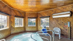 A wooden cabin with a hot tub, two windows, a chair, and a sign.