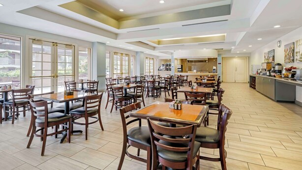 A spacious dining area with multiple tables and chairs, large windows, and a kitchen in the background.