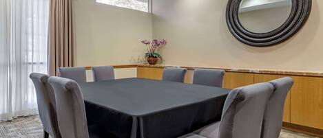 A conference room with a large table, six chairs, a potted plant, a round mirror, and a window with curtains.