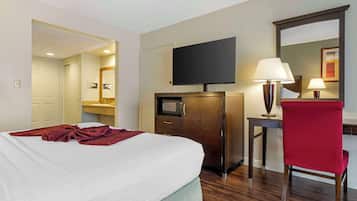 A hotel room with a bed, a desk with a lamp, a television, and a mirror.