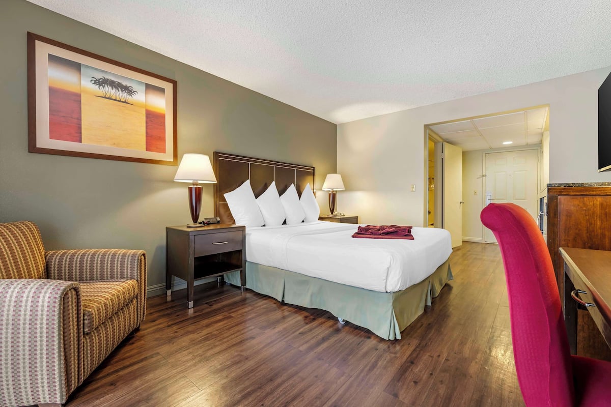 A hotel room with a bed, two bedside tables with lamps, a chair, a desk, and a framed picture on the wall.