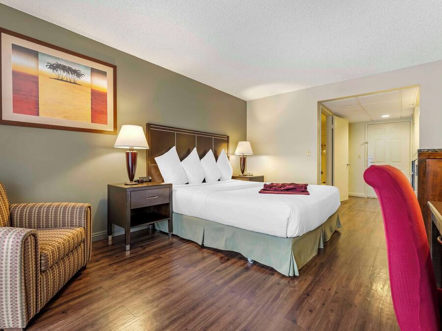 A hotel room with a bed, two bedside tables with lamps, a chair, a desk, and a framed picture on the wall.