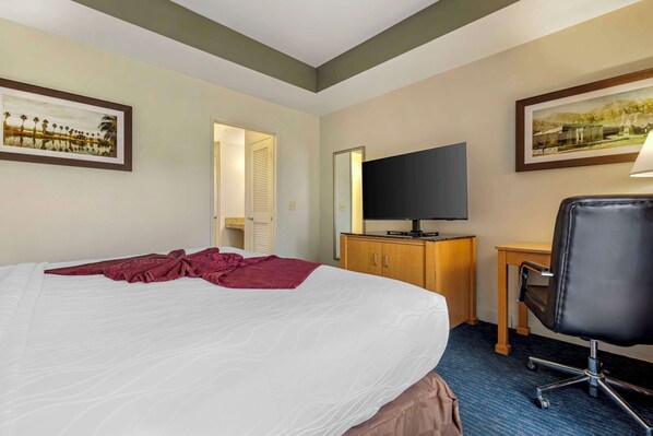 A hotel room with a large bed, a television on a wooden cabinet, a desk with a chair, and two framed pictures on the walls.