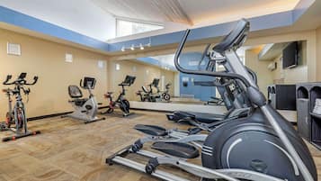 A gym with various exercise equipment, including treadmills and stationary bikes, arranged in a spacious layout with a high ceiling and large windows.