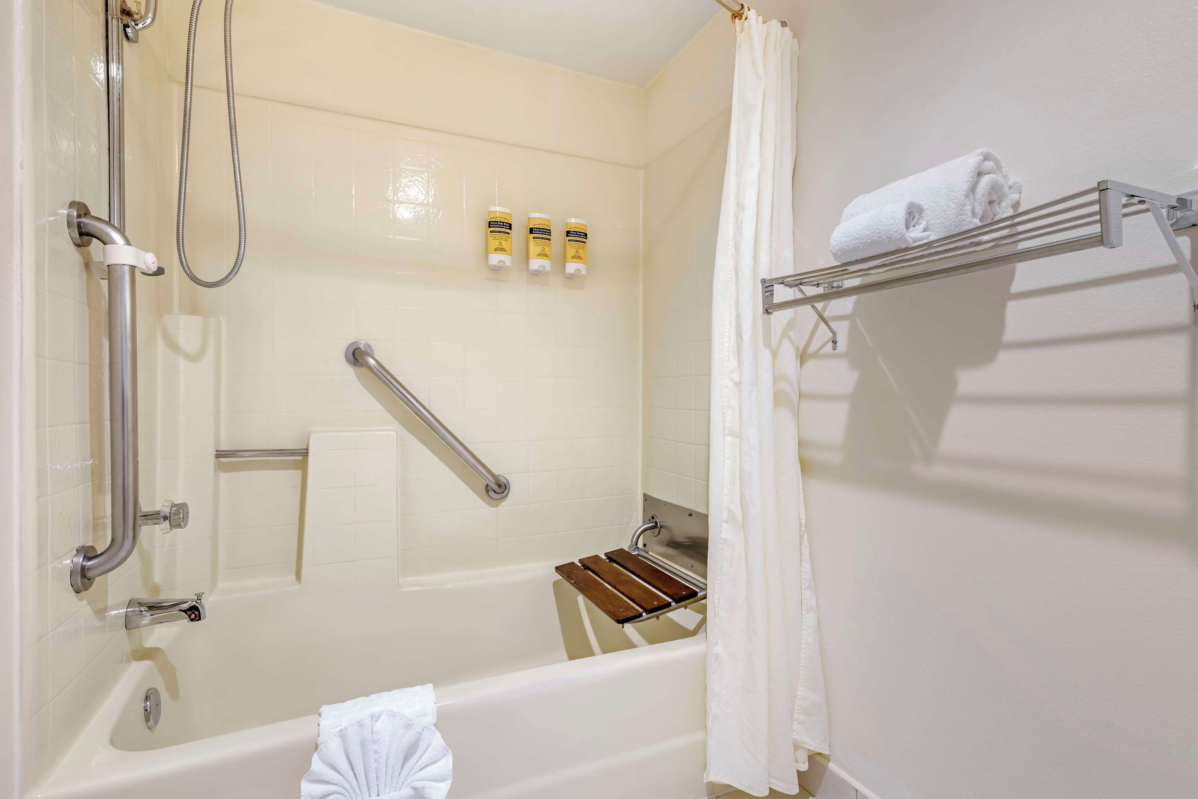 Un baño con bañera, ducha, baranda, toallero y estante con artículos de aseo.