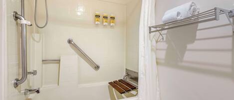 A bathroom with a bathtub, a shower, a handrail, a towel rack, and a shelf with toiletries.