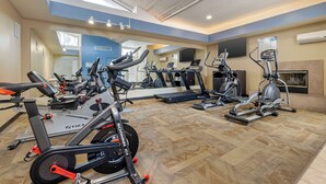 A gym with various cardio and strength training equipment, a large mirror, and a ceiling with skylights.