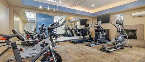 A gym with various cardio and strength training equipment, a large mirror, and a ceiling with skylights.