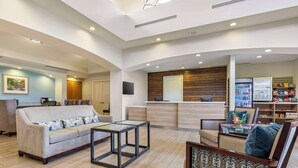 A spacious lobby with a sofa, chairs, a coffee table, a wooden reception desk, and a refrigerator stocked with beverages.