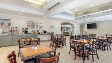 Un restaurant spacieux, doté de nombreuses tables et chaises, d’un espace cuisine et d’une horloge au mur.