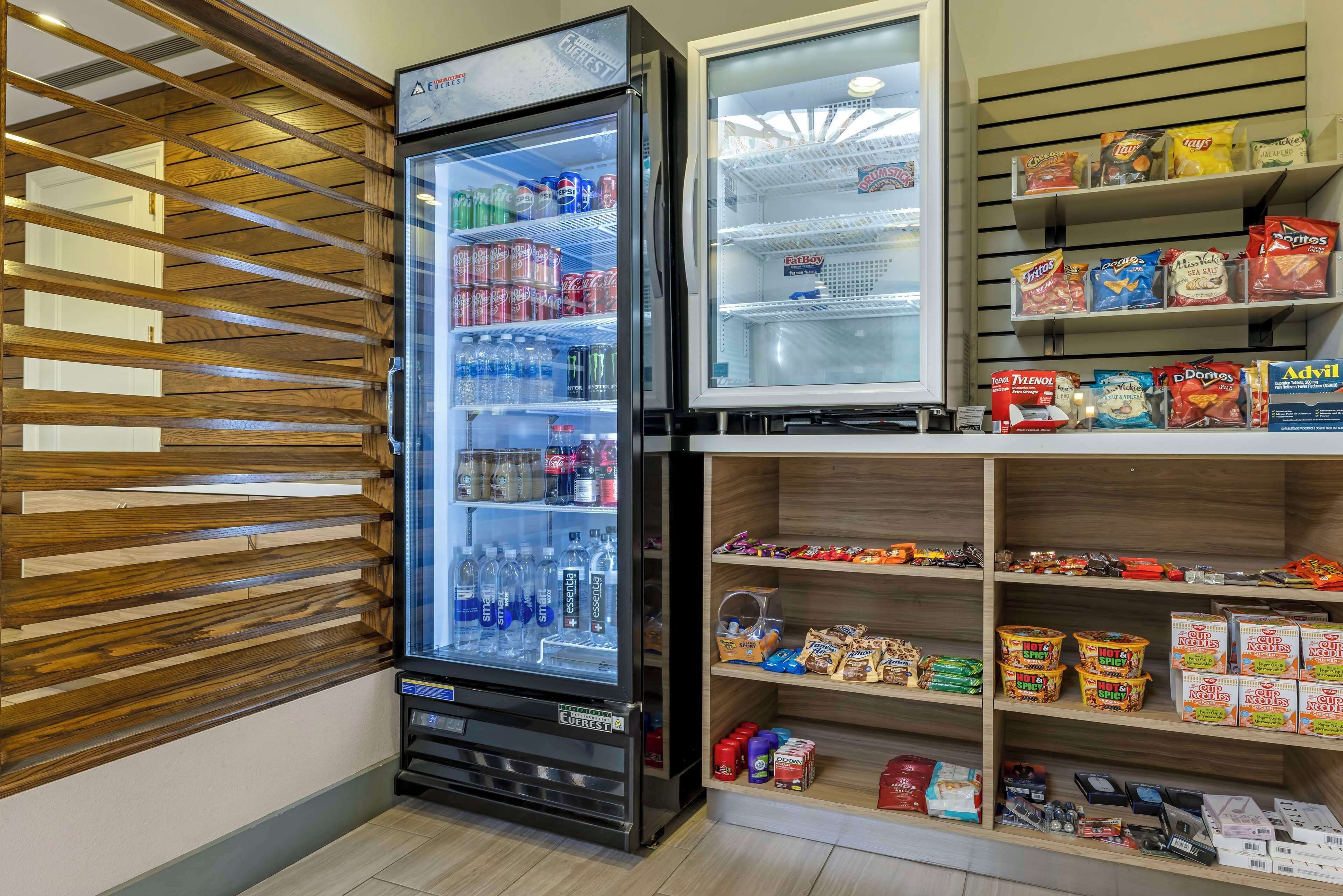 En automattankstation med drycker och snacks, ett kylskåp med en hylla för att visa upp varorna och hyllor med förpackade livsmedel.