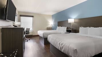 A hotel room with two beds, a desk with a chair, a flat-screen TV, and a window with blinds.