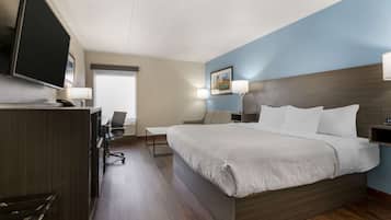 Ein Hotelzimmer mit einem großen Bett, einem Schreibtisch mit Stuhl, einem Fernseher und einem Fenster.