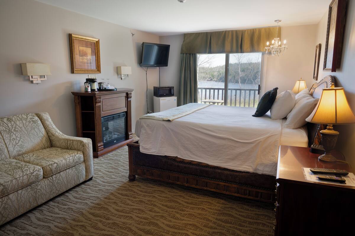 Habitación de hotel con cama, televisión, escritorio con lámpara, silla y vistas al exterior.