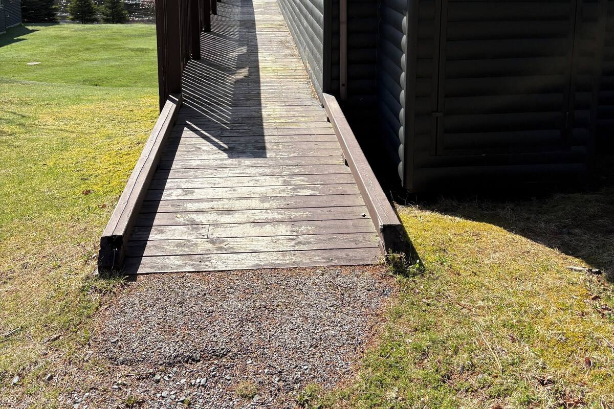 Una terraza de madera que lleva a una cabaña con el número '6A' en el lateral, rodeada de césped y árboles.