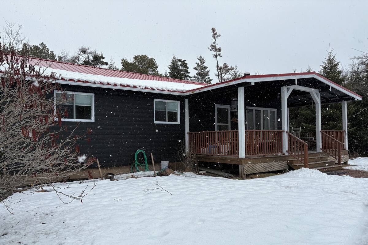 Una casa con porche, techo rojo y suelo cubierto de nieve.