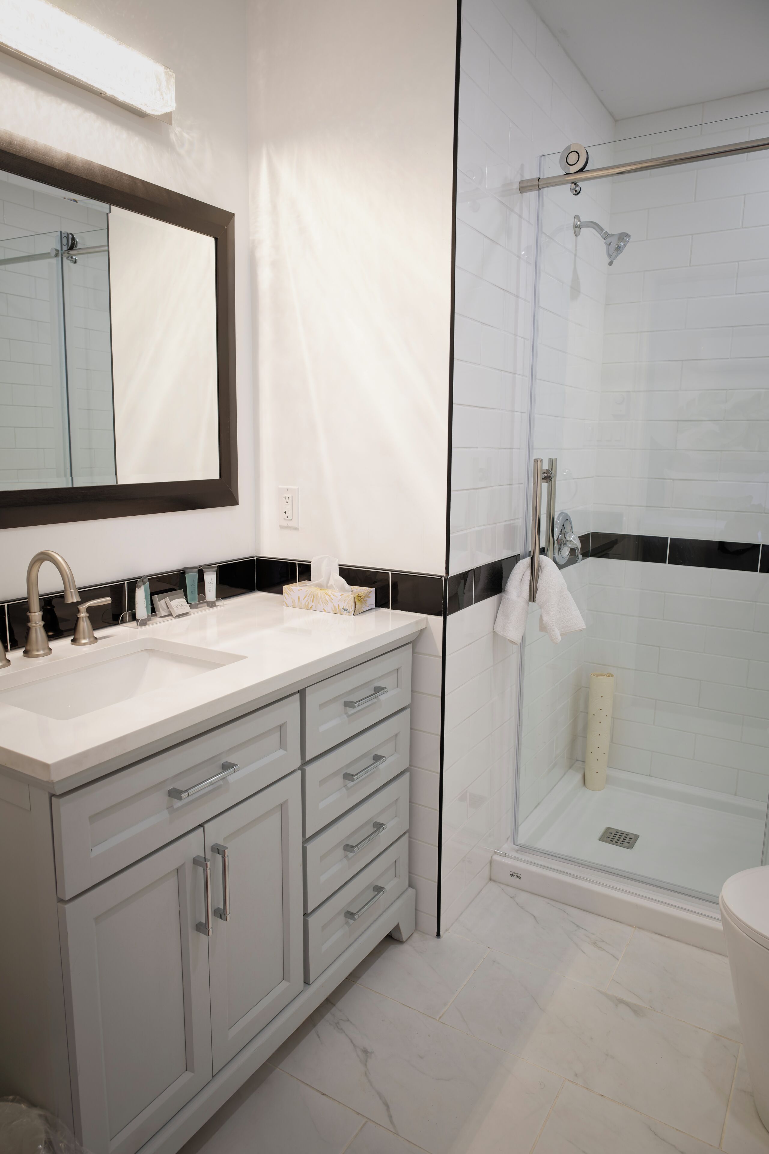 Un baño moderno con ducha envuelta en vidrio, un espejo grande y un lavabo blanco sobre encimera negra.