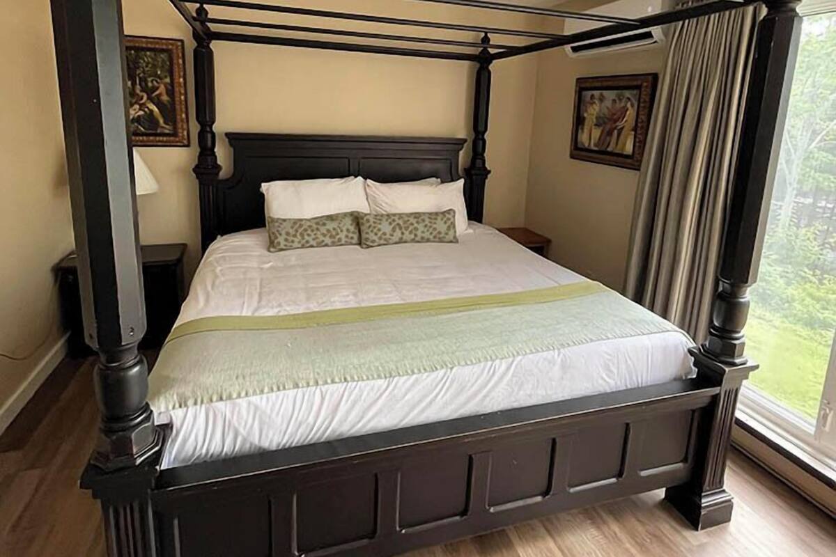 Una cama con dosel de madera oscura, ropa de cama blanca y una manta verde.