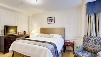 Une chambre d’hôtel avec un grand lit, une télévision, un bureau avec une lampe et un fauteuil à motifs.